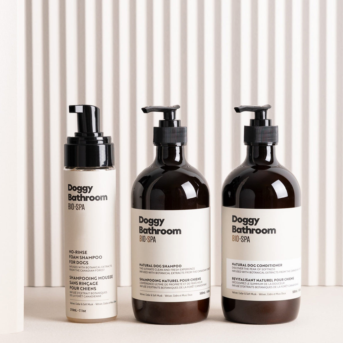 Three Doggy Bathroom Bio-SPA pet care bottles arranged on a white surface against a white slatted background: a beige pump bottle on the left, a dark amber bottle in the center, and a dark amber bottle on the right.